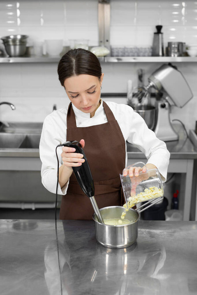 Female pastry chef whips up a mirror icing with white chocolate for a cake with a blender - Foto, immagini