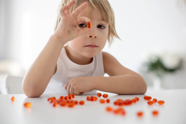 Cute little child, toddler boy, eating alfa omega 3 child suplement vitamin pills at home for better imunity - Foto, Imagem