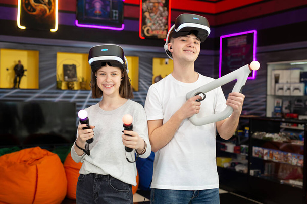 Portrait of teenagers, a boy and a girl with a virtual reality headset in glasses and hand movement controllers in a game club - Fotografie, Obrázek