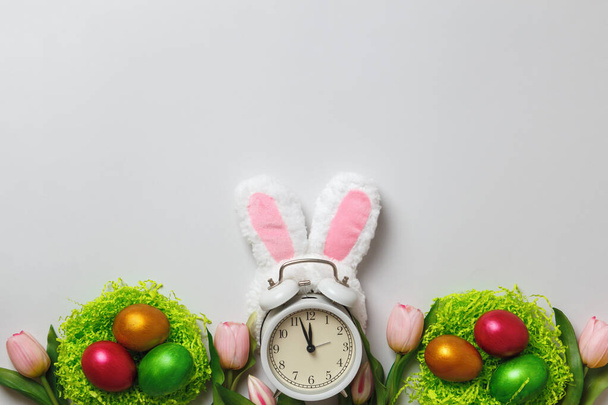 Easter concept. Multi-colored pearl eggs in nests flowers tulips alarm clock on a gray background. Copy space - Foto, Bild