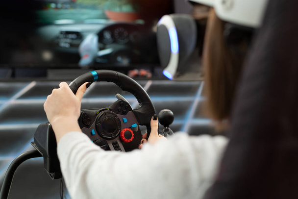 Close-up of the hands of a teenage girl in virtual reality glasses, who is holding the steering wheel and playing a computer game on the console - Fotó, kép