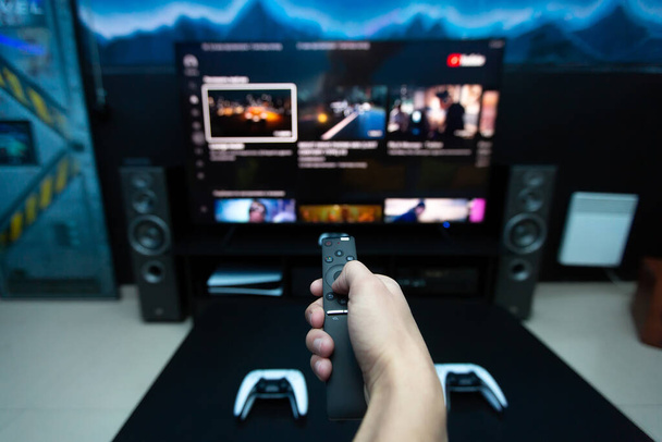 Close-up of a hand with a remote control from the console, choosing a computer game on a large TV - Fotó, kép