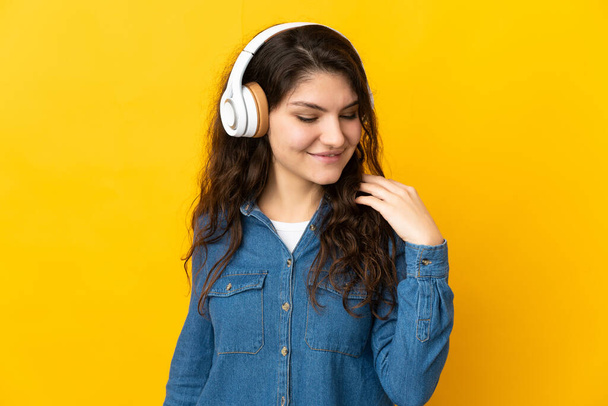 Genç Rus kız sarı arka planda izole edilmiş müzik dinliyor. - Fotoğraf, Görsel