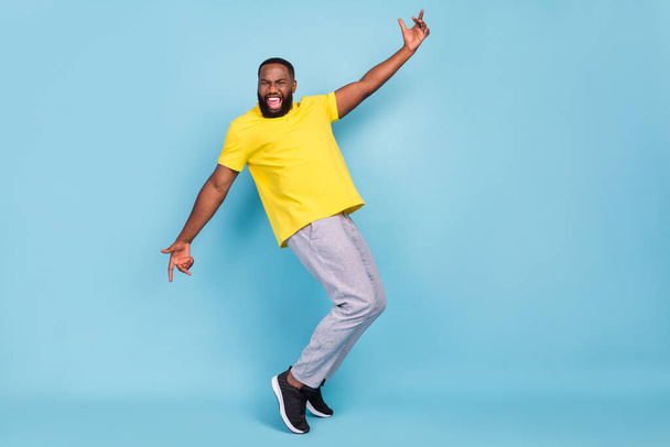 Photo of excited funny dark skin guy dressed yellow t-shirt dancing smiling isolated blue color background - Zdjęcie, obraz