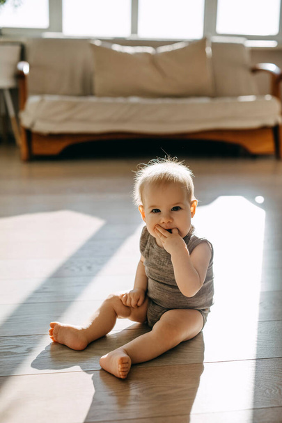 Barefoot baby zitten op de vloer thuis, zuigen vingers. - Foto, afbeelding
