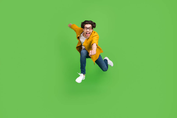 Photo of funny funky young man wear yellow shirt spectacles smiling jumping running fast isolated green color background - Foto, immagini