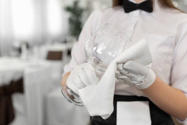 Großaufnahme eines Glases und eines Handtuchs in den Händen eines Kellners. Vorbereitung, Tischdekoration - Foto, Bild