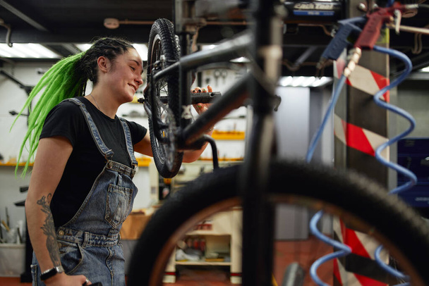 Cheerful mechanic repairing bicycle in workshop - 写真・画像