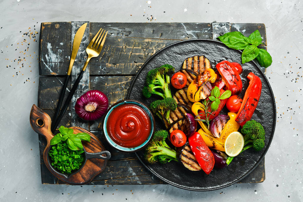 Grilled vegetables (colorful bell pepper, zucchini, eggplant, cherry tomatoes and broccoli) on a black stone plate. Top view. Rustic style. - Фото, изображение