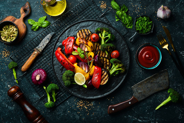 Grilled vegetables (colorful bell pepper, zucchini, eggplant, cherry tomatoes and broccoli) on a black stone plate. Top view. Rustic style. - Zdjęcie, obraz