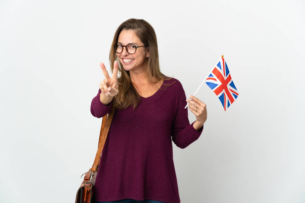 Mulher brasileira de meia idade segurando uma bandeira do Reino Unido isolada em fundo branco sorrindo e mostrando sinal de vitória - Foto, Imagem