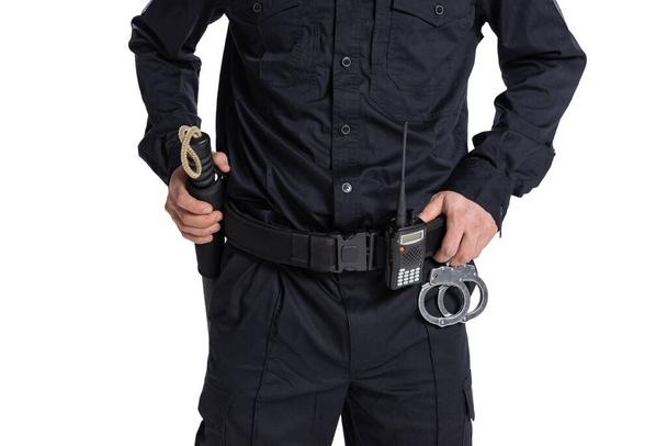 Gehakt beeld van mannelijke politieagent in zwart uniform met walkie-talkie en handboeien geïsoleerd op witte achtergrond. - Foto, afbeelding