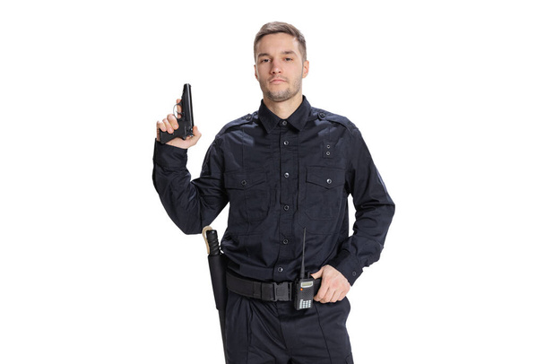 Half-length portrait of young male policeman officer wearing black uniform posing with gun isolated on white background. Concept of job, caree, law and order. - Fotó, kép