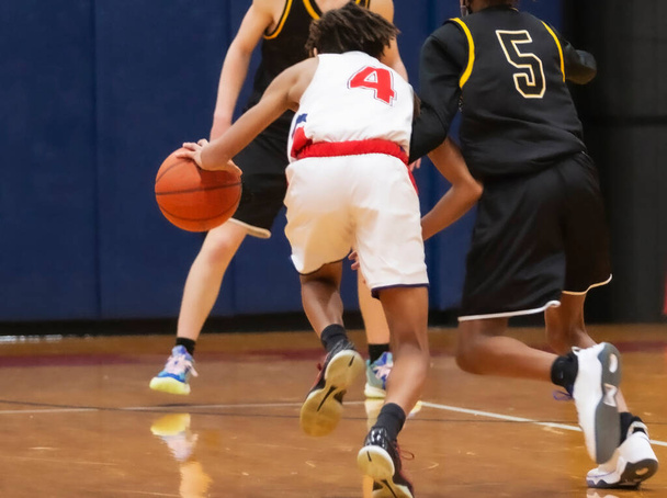 Visão traseira de um jogador de basquete do ensino médio driblando a bola em direção aos defensores durante um jogo. - Foto, Imagem