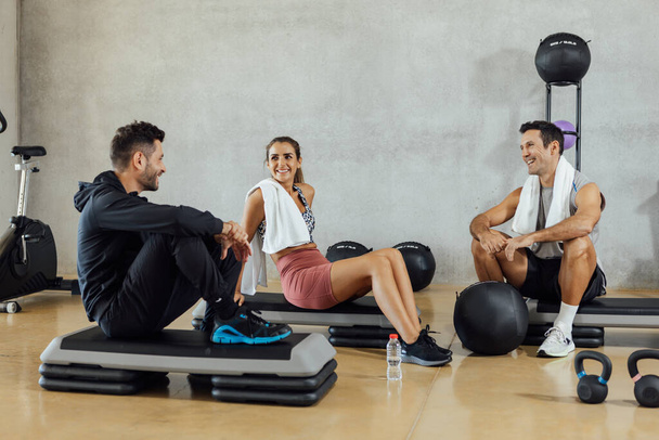 Fröhliche Gruppe von Freunden unterhält sich während einer Pause im Fitnessstudio.  - Foto, Bild