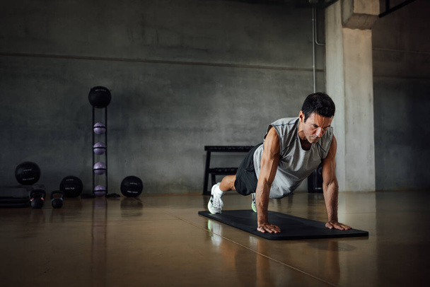 Athletic man doing pushups exercise at dark gym. - Photo, Image