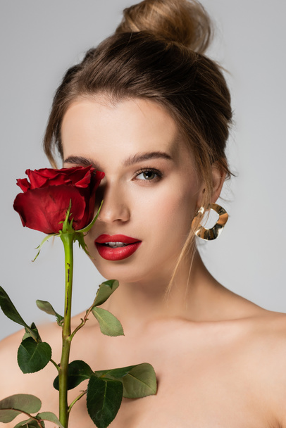 charming woman with makeup holding red rose near face isolated on grey - Foto, Bild