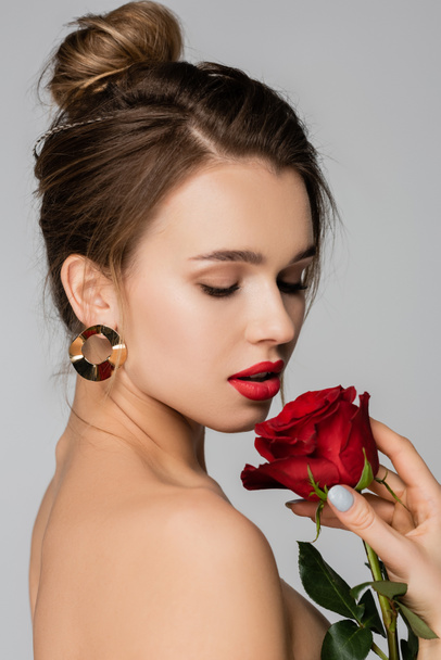 pretty woman in golden earring holding red rose isolated on grey - Photo, Image