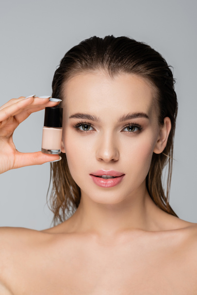 young woman with natural makeup holding face foundation isolated on grey - Фото, зображення