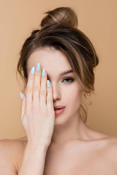 young woman obscuring face with hand while looking at camera isolated on beige - Photo, Image