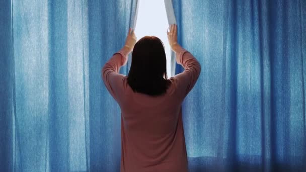 Guten Morgen Konzept - Rückansicht einer jungen Frau im Pyjama, die zu Hause oder im Hotel Vorhänge öffnet - Filmmaterial, Video