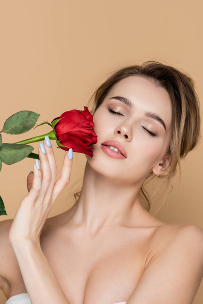 pretty woman with naked shoulders and natural makeup near red rose isolated on beige - Foto, Imagem