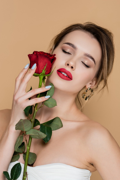 pretty woman in strapless top holding rose near face with red lips isolated on beige - Foto, imagen