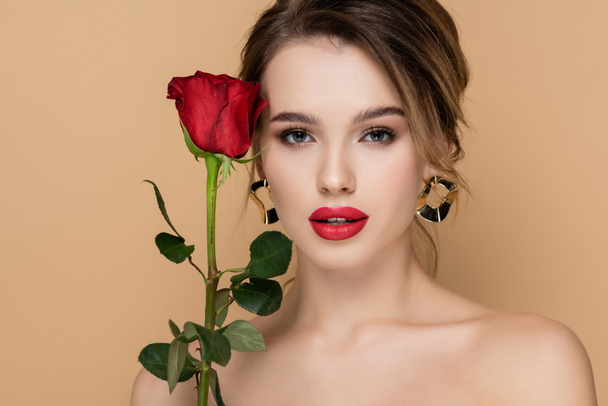charming woman with red lips and fresh rose looking at camera isolated on beige - Photo, Image