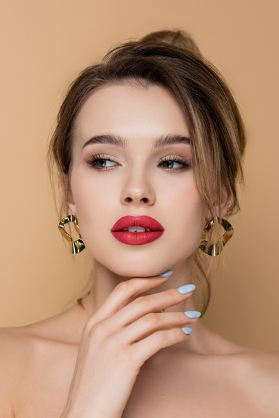 pretty woman with makeup and golden earrings looking away isolated on beige - Fotó, kép