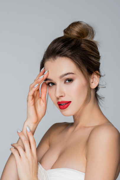 pretty woman with red lips looking at camera while touching face isolated on grey - Photo, Image