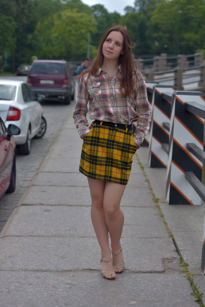 slender pretty brunette girl in a plaid blouse and skirt on a city street - Zdjęcie, obraz