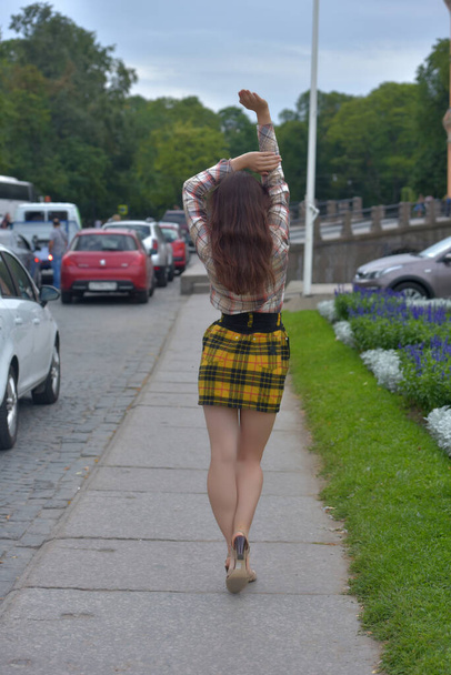slender pretty brunette girl in a plaid blouse and skirt on a city street - Photo, Image