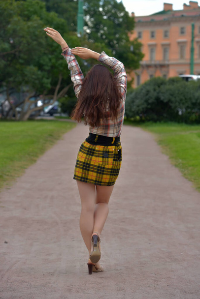 slender pretty brunette girl in a plaid blouse and skirt on a city street - Foto, imagen