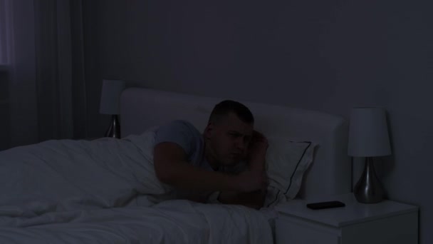 young man waking up to turn off alarm clock on his smartphone and going back to sleep  - Footage, Video