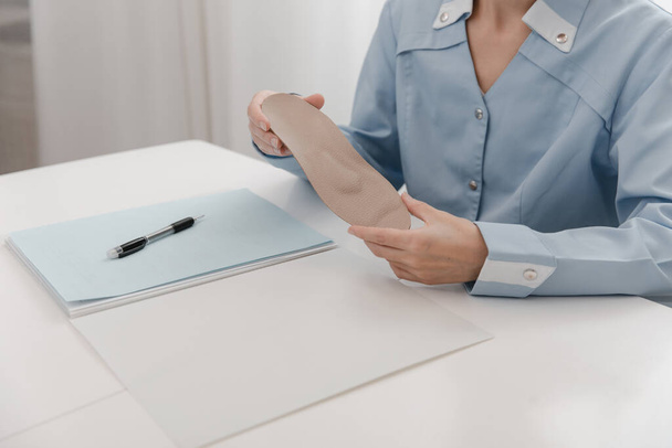 Doctor holding an insole while sitting at a table. Orthopedist tests the medical device. Orthopedic insoles. Foot care. Flat Feet Correction. Treatment and prevention of flat feet and foot diseases - Photo, image