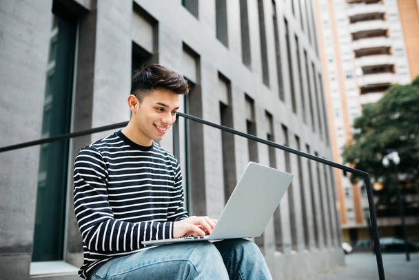 Молодой человек, сидит на улице, используя ноутбук - Фото, изображение