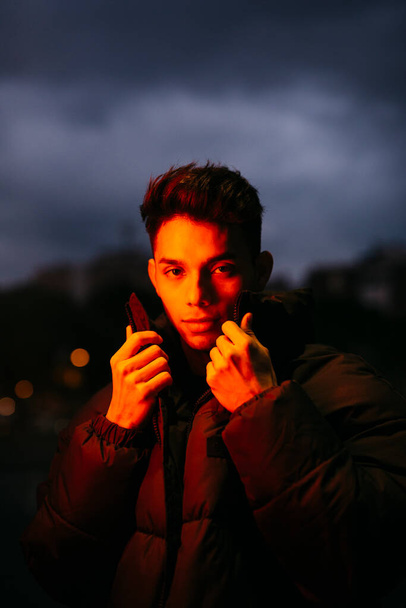 赤い光の下で黒いコートを着た若い男の肖像画 - 写真・画像
