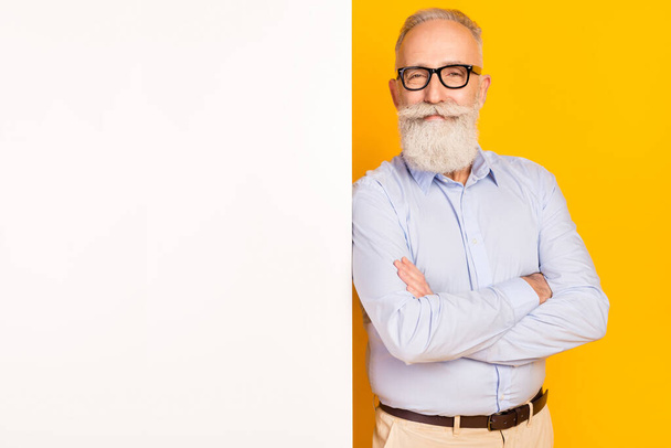 Fénykép a vonzó édes kor úriember viselni kék ing szemüveg karok keresztbe fehér üres tér elszigetelt sárga háttér - Fotó, kép