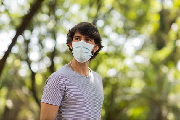 Portrait of a handsome man wearing a medical protective mask on his face on a sunny day at park. High quality photo. Urban life. - Foto, Bild