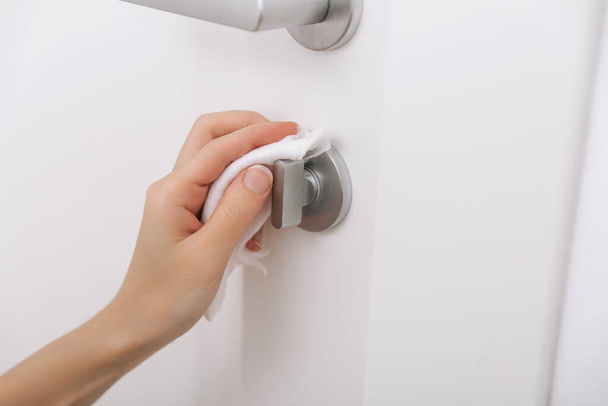 Cleaning door handles with an antiseptic wet wipe and gloves. Sanitize surfaces prevention in hospital and public spaces against corona virus. Woman hand using towel for cleaning home room door link - Valokuva, kuva