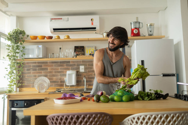 Happy and healthy young man meal prepping whole vegetarian meal in the kitchen. High quality photo. Feel good, healthy and health concept.  - 写真・画像