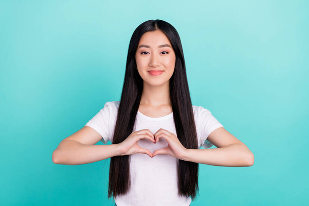 Retrato de atractiva chica de pelo largo alegre mostrando afecto símbolo del corazón aislado sobre fondo de color turquesa brillante verde azulado - Foto, imagen