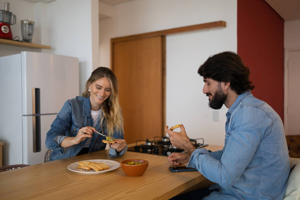 A las parejas jóvenes les encanta comer una ensalada de guacamole súper saludable con tostadas enteras en la cocina. Foto de alta calidad. Concepto alimenticio - Foto, Imagen