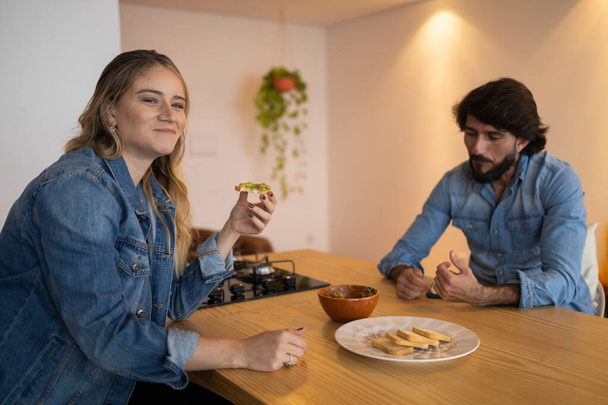 Birbirine aşık genç bir çift çok sağlıklı bir guacamole salatası yiyor ve bütün tostu mutfakta yiyor. Yüksek kalite fotoğraf. Yiyecek konsepti - Fotoğraf, Görsel