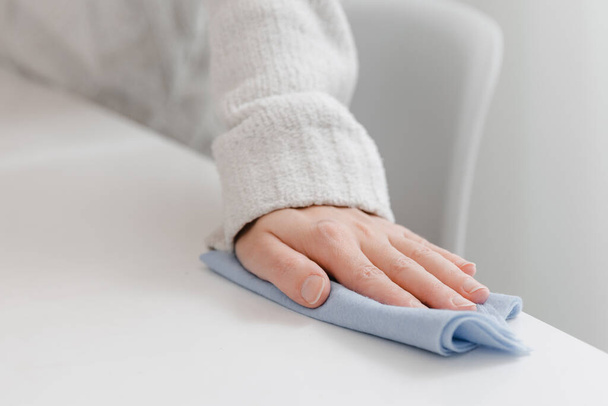 Cleaning the table with a blue microfiber cloth. Sanitize surfaces prevention in hospital and public spaces against coronavirus. Woman hand using wet wipe at home. Cleaning the room - Фото, зображення