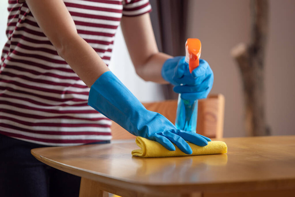 Primer plano de las manos de ama de casa femenina en guantes de goma con spray limpiando la mesa en la sala de estar en casa, concepto de limpieza feliz - Foto, imagen
