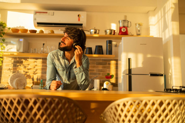 Widok młodego człowieka słuchającego muzyki ze słuchawkami w uszach w kuchni swojego mieszkania. Wysokiej jakości zdjęcie. Telefon komórkowy, technologia, muzyka, miejskie życie, czuć się dobrze. - Zdjęcie, obraz