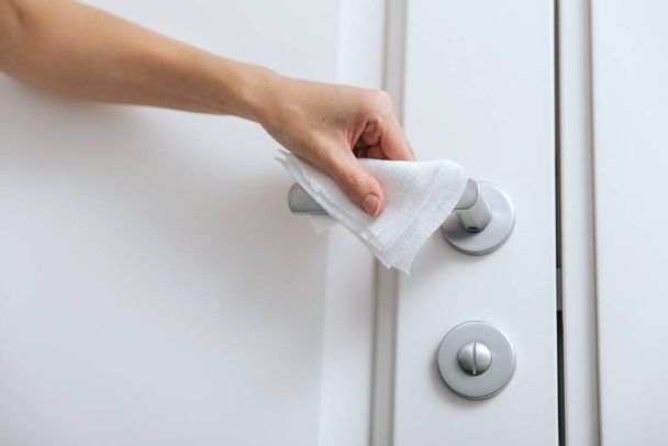 Cleaning door handles with an antiseptic wet wipe and gloves. Woman hand using towel for cleaning home room door link. Sanitize surfaces prevention in hospital and public spaces against corona virus - Foto, imagen