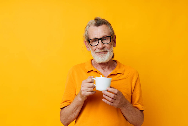 elderly man in a yellow t-shirt white mug yellow background - Foto, Bild