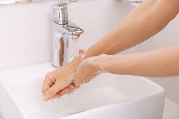 Washing hands under the flowing water tap. Washing hands rubbing with soap for corona virus prevention, hygiene to stop spreading corona virus in or public wash room. Hygiene concept hand detail - Φωτογραφία, εικόνα